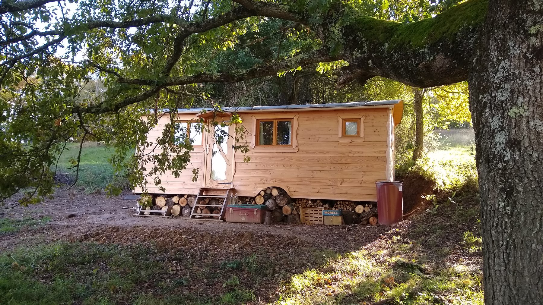 Roulotte en bois sous les arbres, finition naturelle