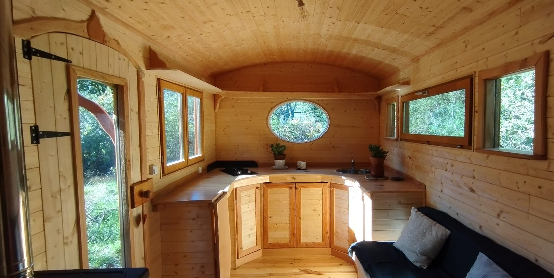 Intérieur roulotte : cuisine en bois avec hublot central